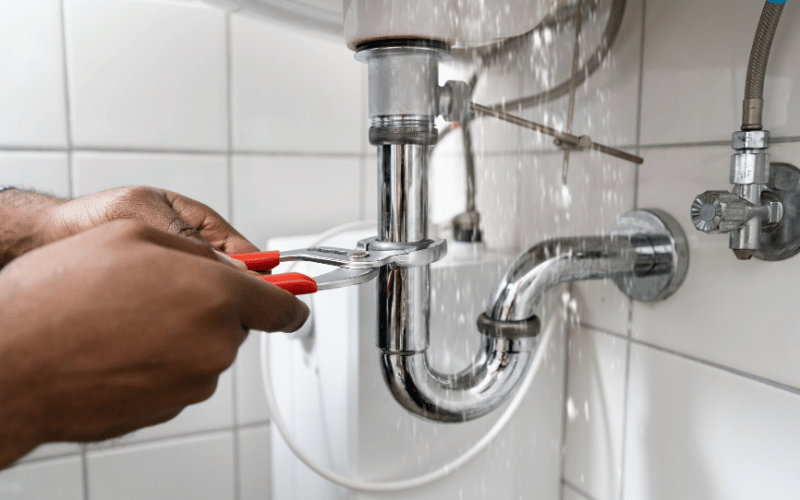 Plombier resserrant un siphon chromé sous un lavabo