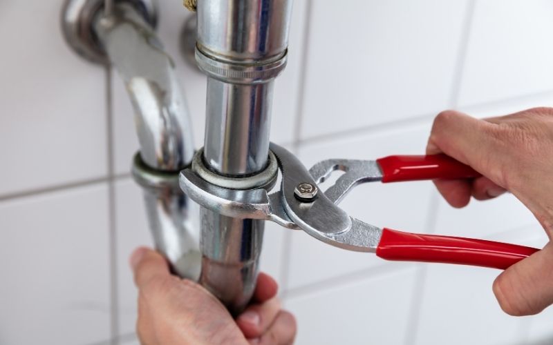 Plombier resserrant en urgence un raccord de siphon avec une pince