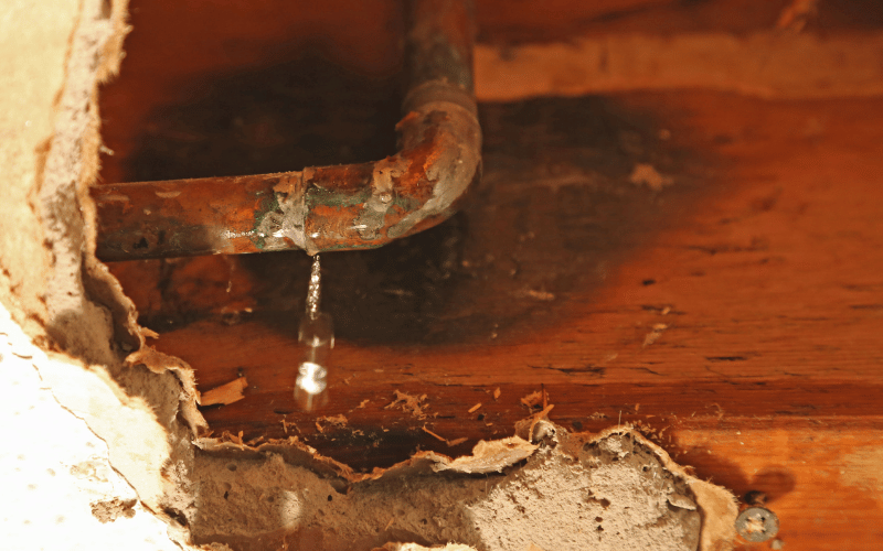 Goutte d'eau tombant d'un tuyau en cuivre encastré dans un mur abîmé