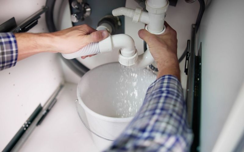Plombier inspectant un siphon qui fuit sous un évier